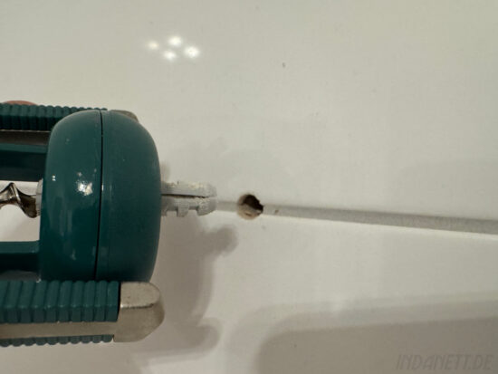 Ein Korkenzieher mit Dübel vor einer Wand mit Loch, in der vorher der Dübel gesteckt hat.