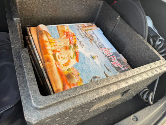 Drei große Pizzaschachteln in einer Thermobox die in einem Kofferraum steht.